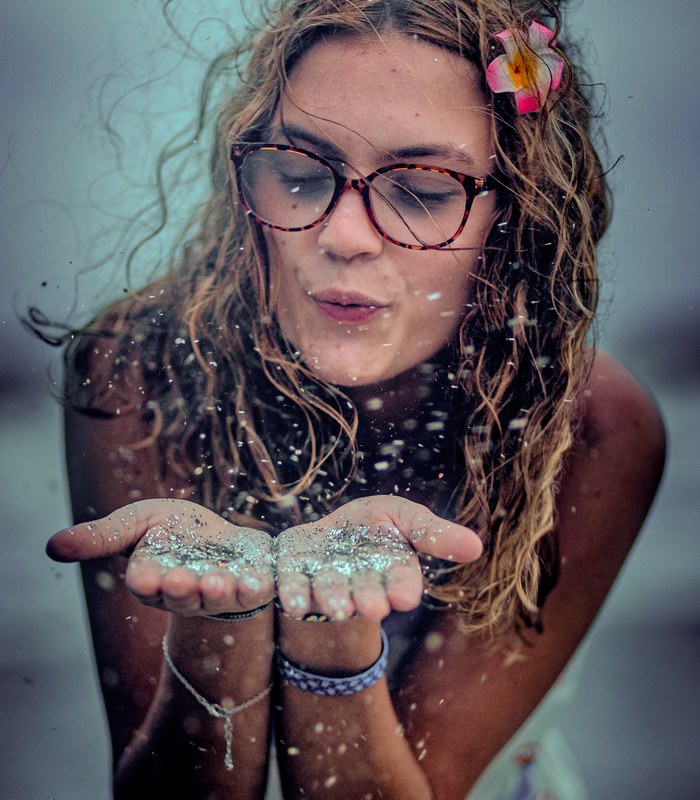 A young woman blowing glitter into the wind at the beach
